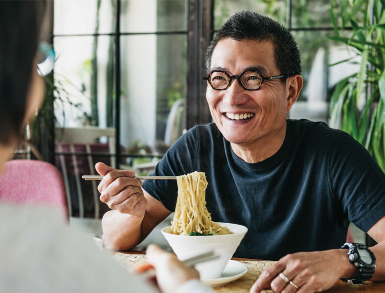 Man in his 50s talking to woman and smiling, freshly made Chinese food, noodle soup, lunch, relaxation