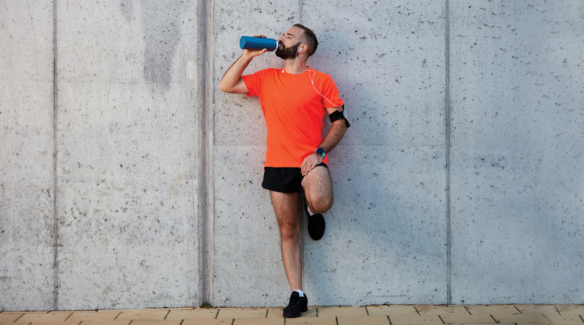 Man resting from running and drinking water while standing against the wall
