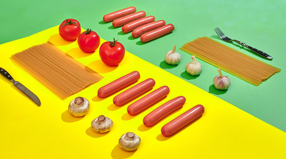 Illustration of ingredients laid out including pasta, tomatoes, mushrooms, sausages, garlic, a knife, and a fork.