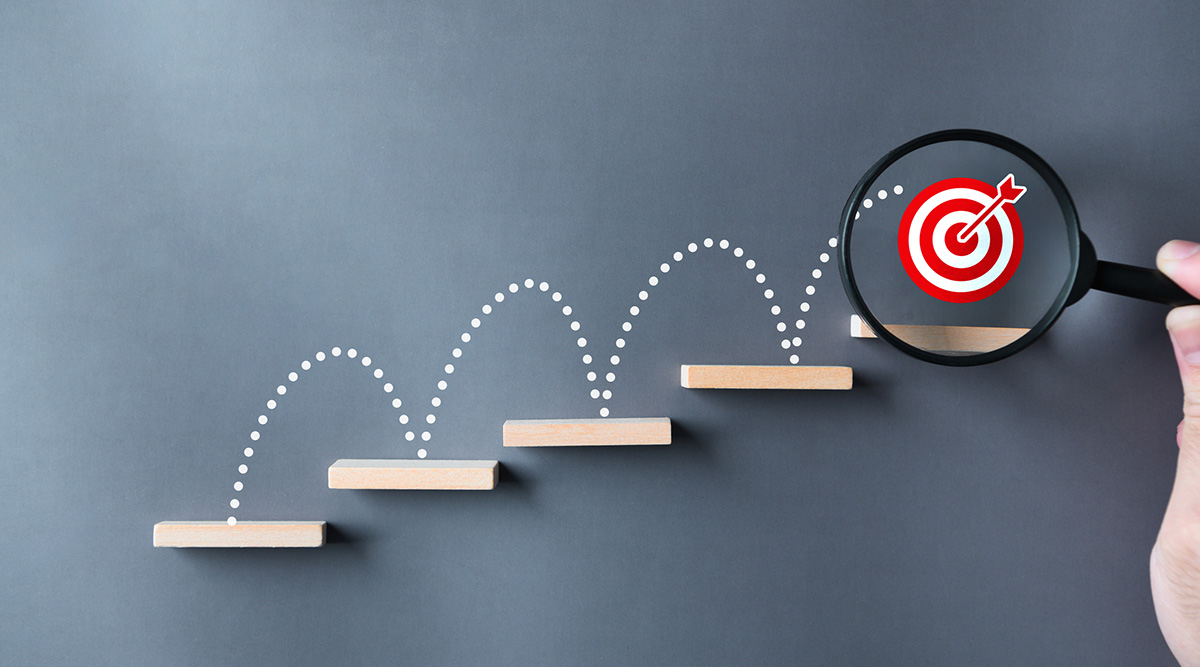 A bullseye target at the top of steps with a magnifying glass over it.