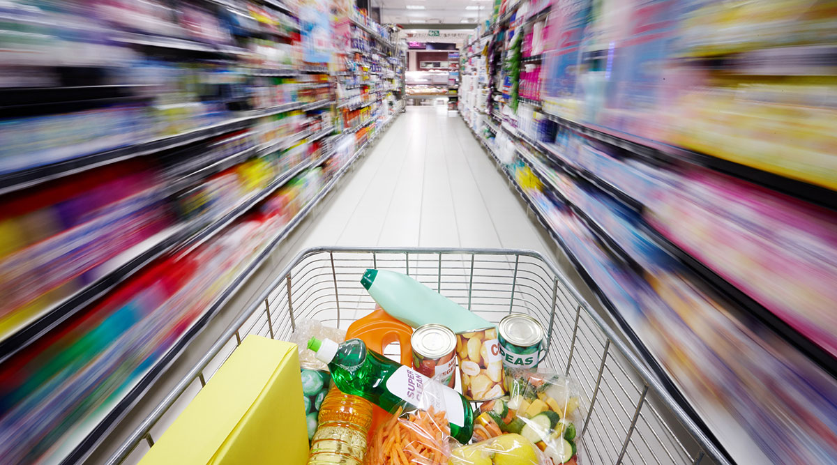 Shopping cart filled with grocery items moving through an aisle of a supermarket