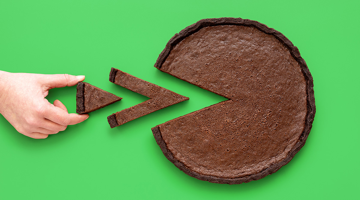 Chocolate care with triangular slices taken out of it and a hand grabbing a piece.