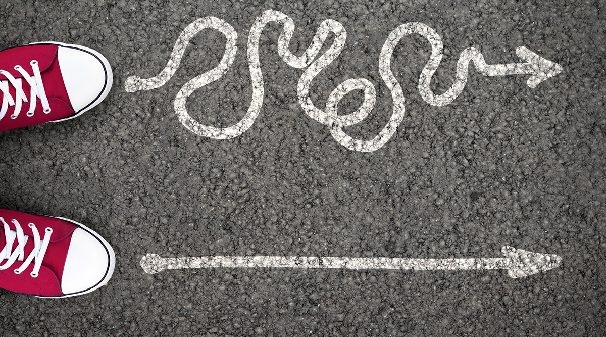 Red sneakers pointing to two different chalk arrows on a road.