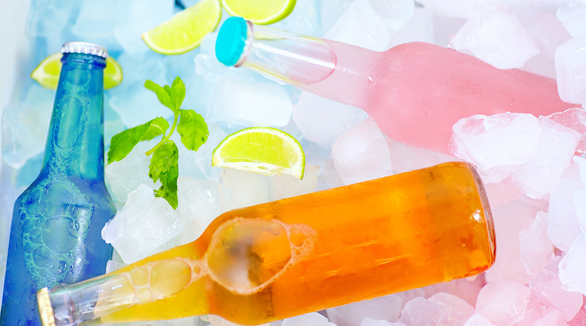 Colorful beverages in glass soda bottles in ice with lime wedges.