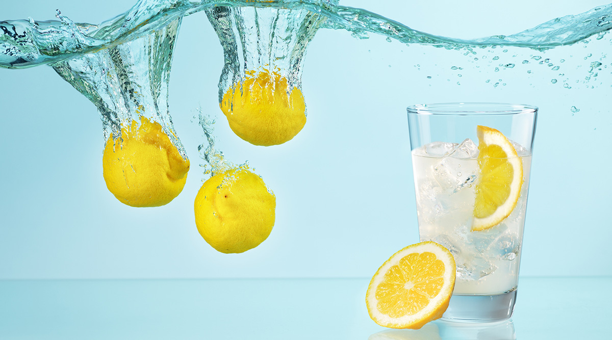 Three whole lemons under water and a glass of water with a lemon wedge.