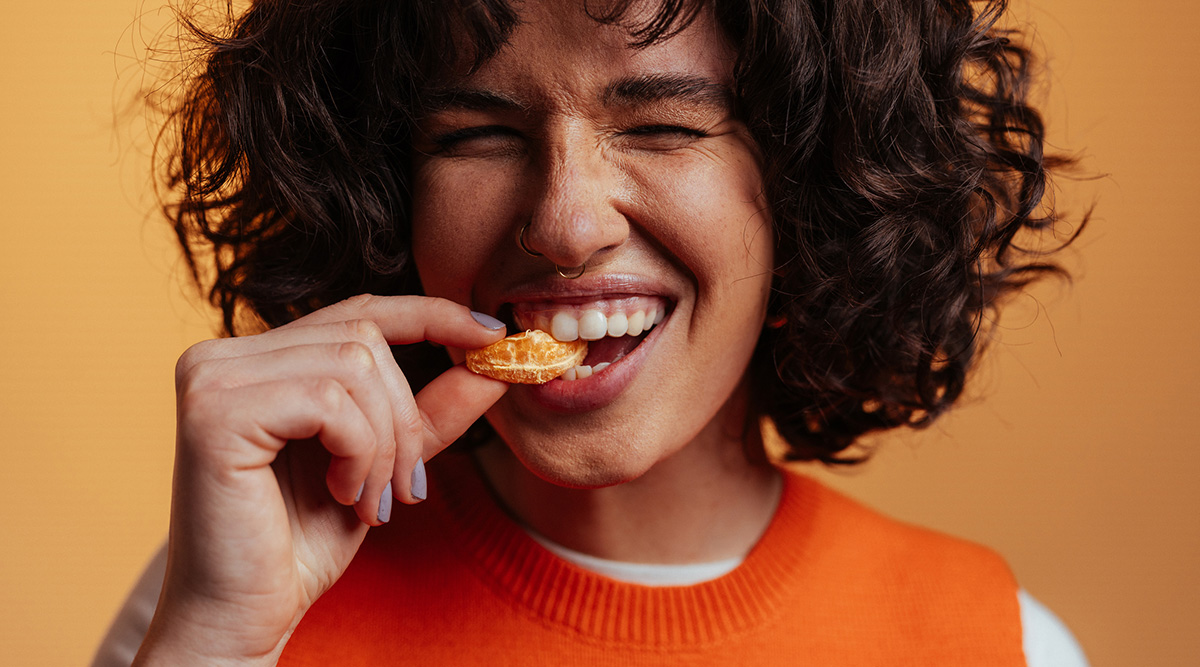 Person smiling while biting into a piece of a clementine