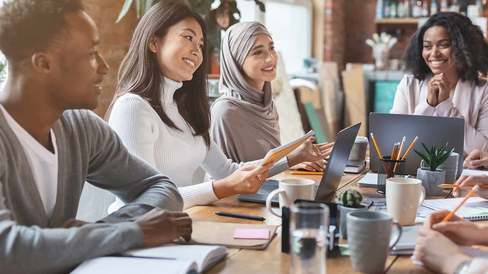 Diverse group of working adults in a meeting at a table with laptops.